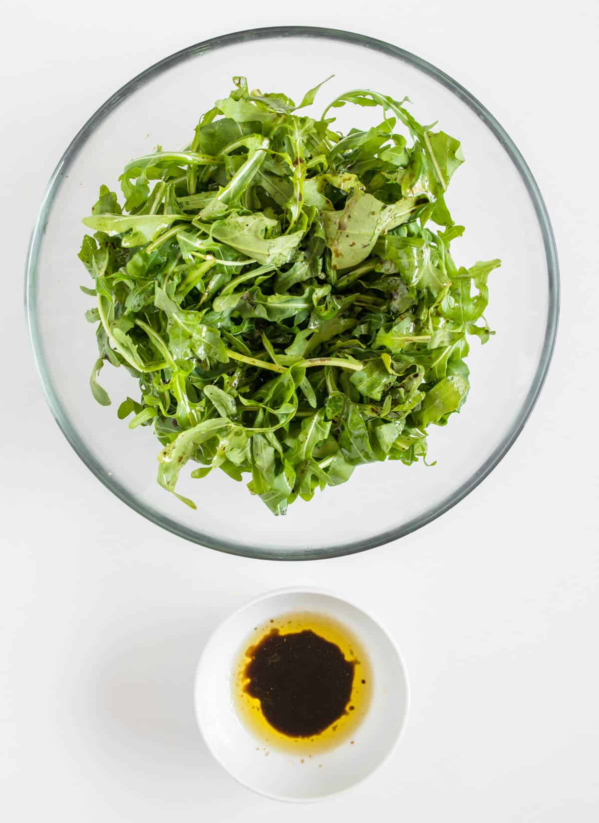 Rocket salad mixed with dressing in a bowl with small bowl of additional dressing