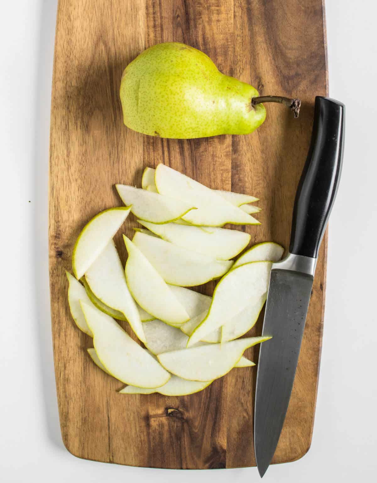 Pear being sliced thinly on a chopping board 
