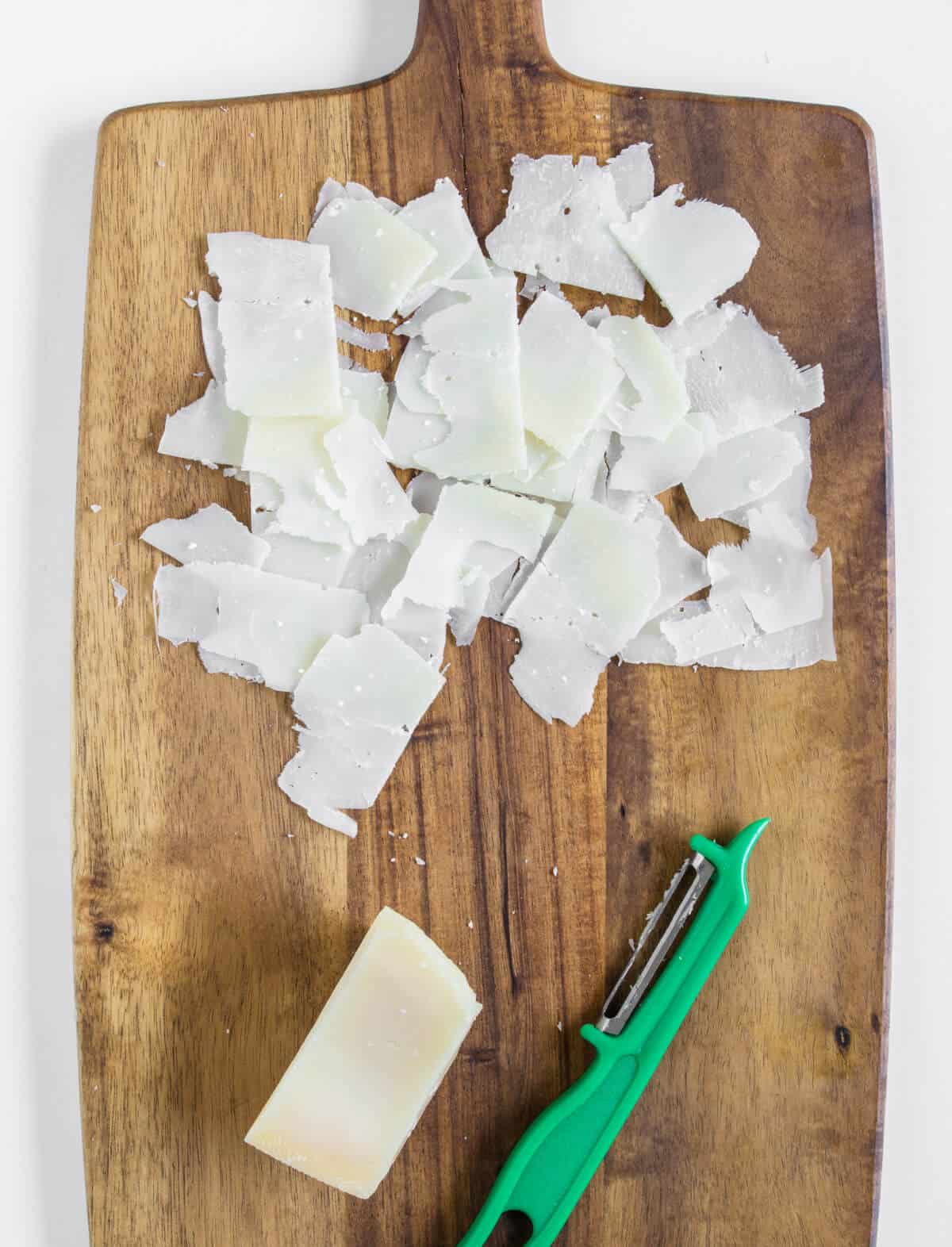 Grated parmesan cheese with a peeler on a chopping board  