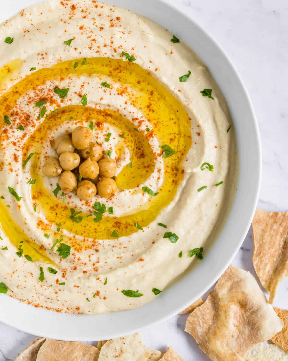 Hummus garnished with paprika, olive oil and parsley along with pita chips