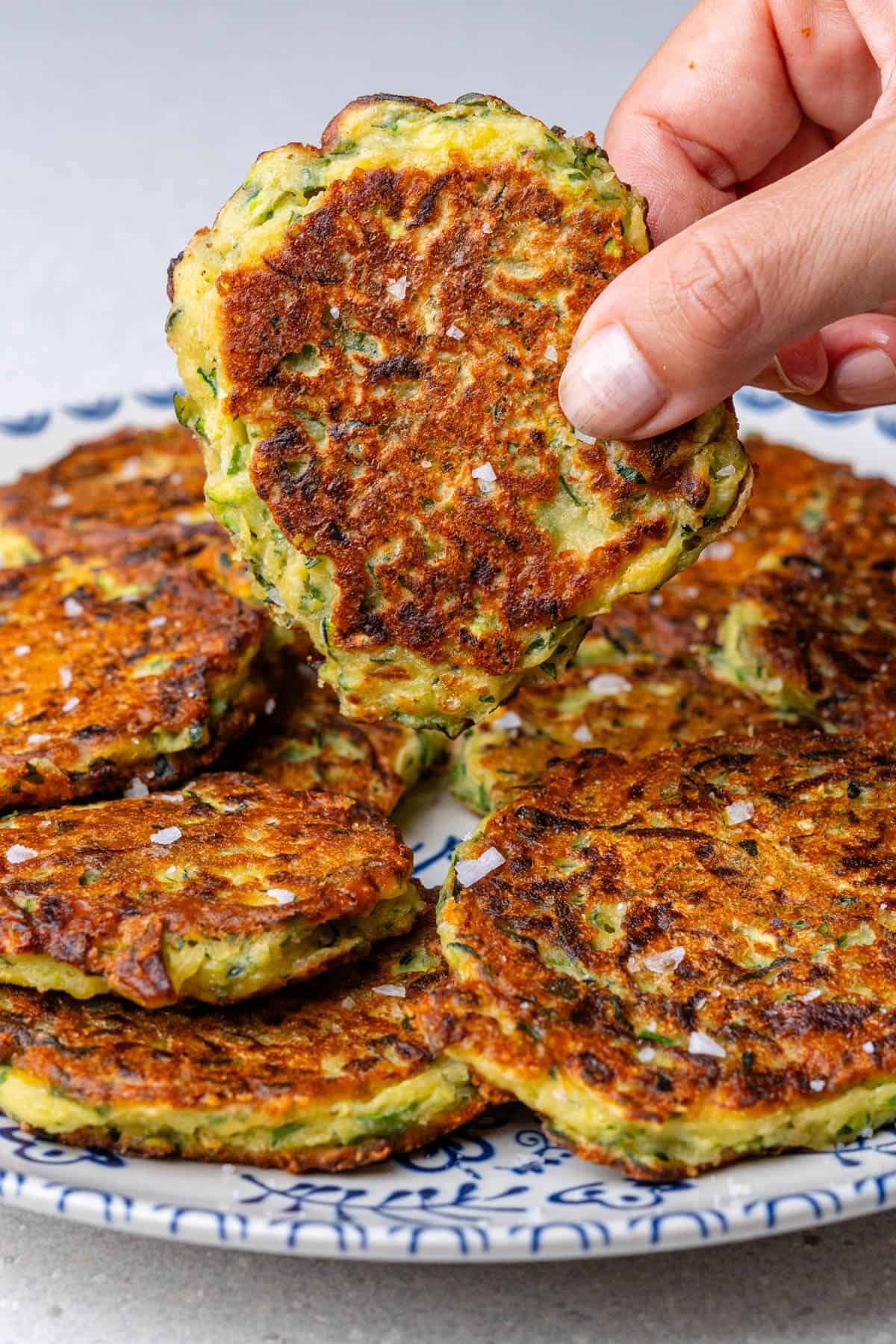 A zucchini fritters being picked up from a plate
