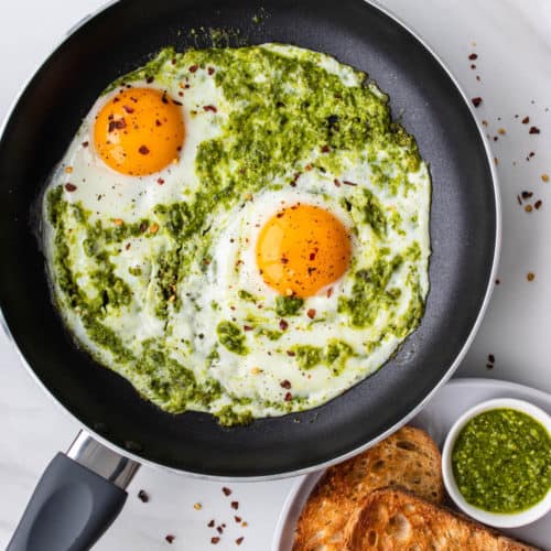Pesto eggs on a fry pan with a side of toast and extra pesto