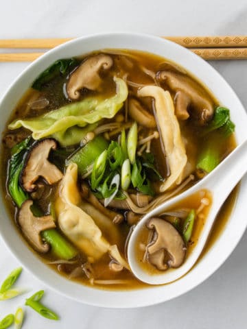 Shiitake broth and dumpling soup in a bowl with serving spoon and chopsticks