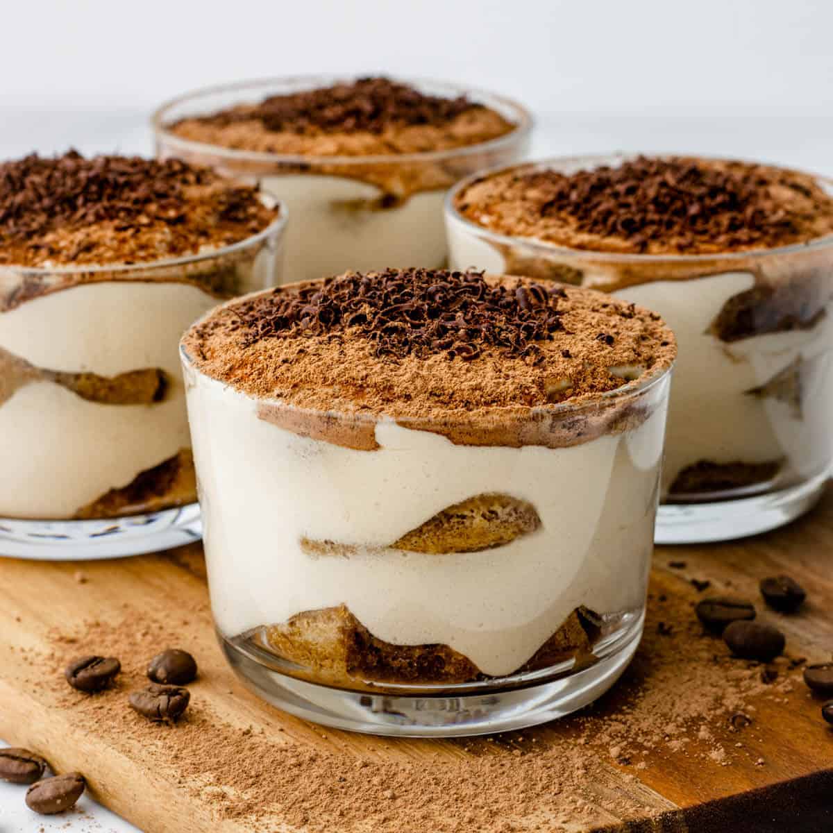 Tiramisu cups on a chopping board topped with cacao and grated chocolate
