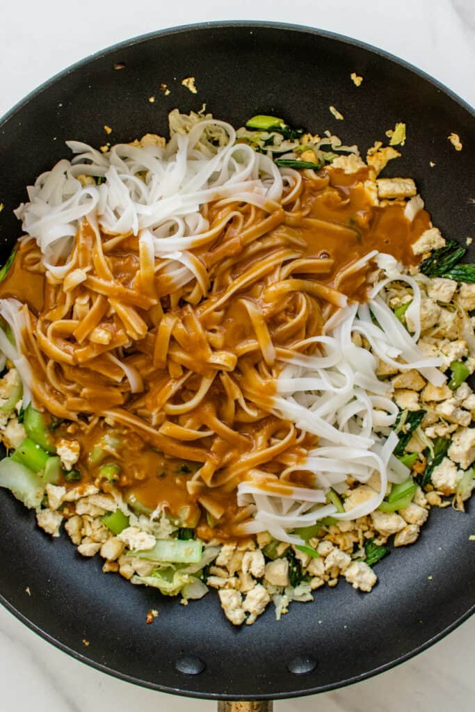 Peanut sauce and noodles added to a fry pan with tofu and veggies