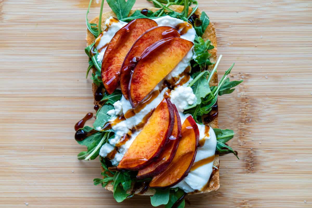 Peaches and balsamic glaze added on toast on how to make burrata toast