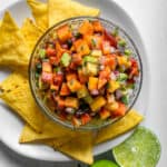 Peach salsa in a bowl served with corn chips and fresh lime