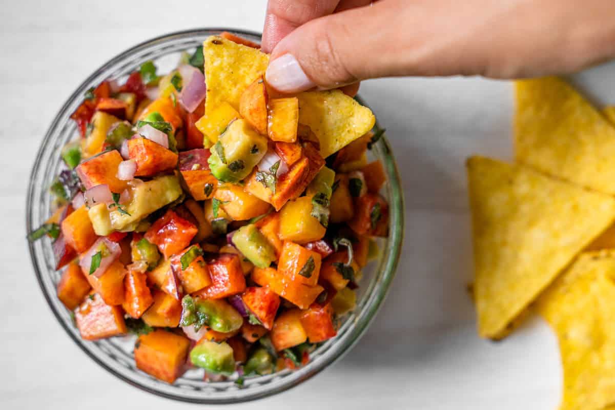 Corn chip being dipped into final peach salsa