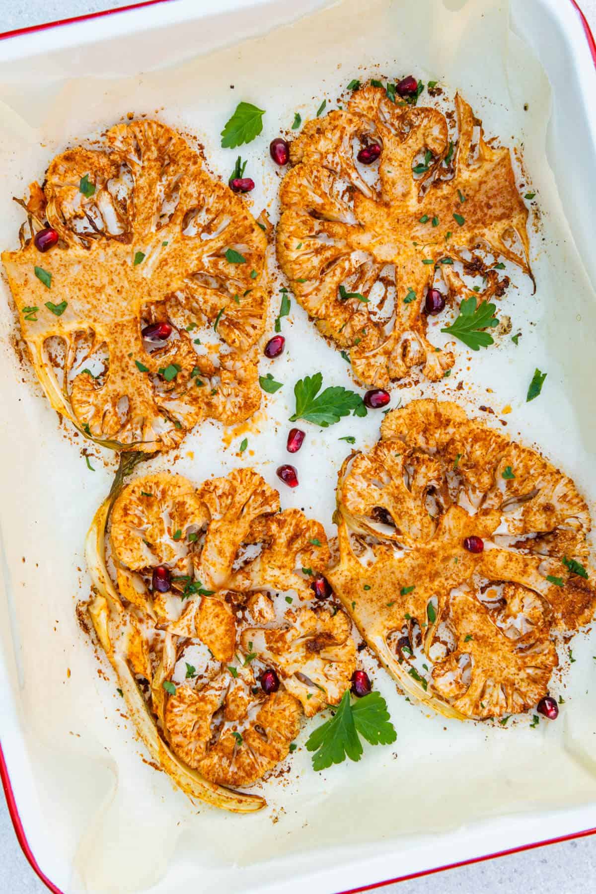 Four roasted cauliflower steaks in an oven tray