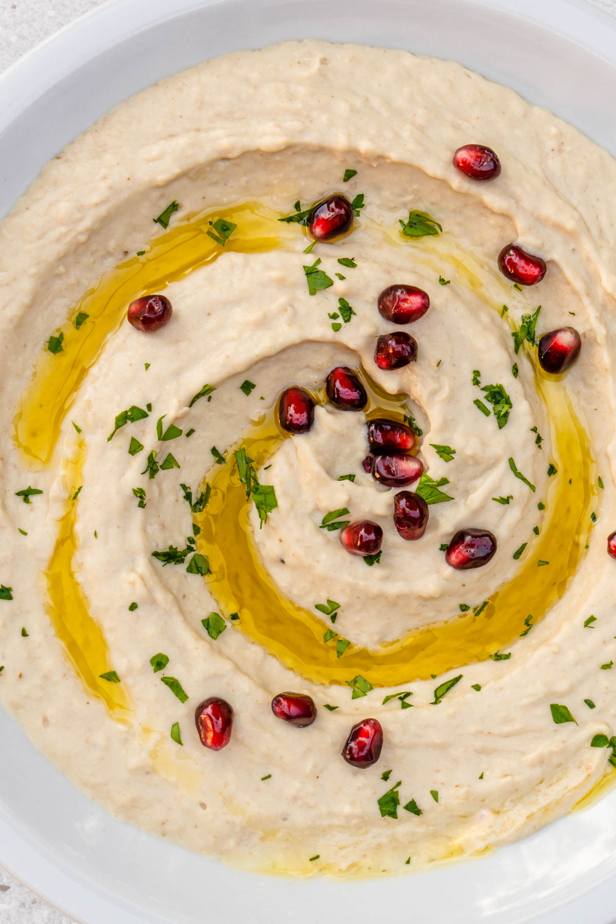 Close up of white bean dip served with pomegranate and parsley