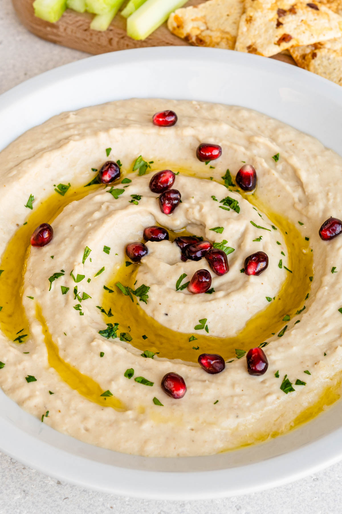 Bowl of white bean dip hummus garnished with pomegranate and parsley