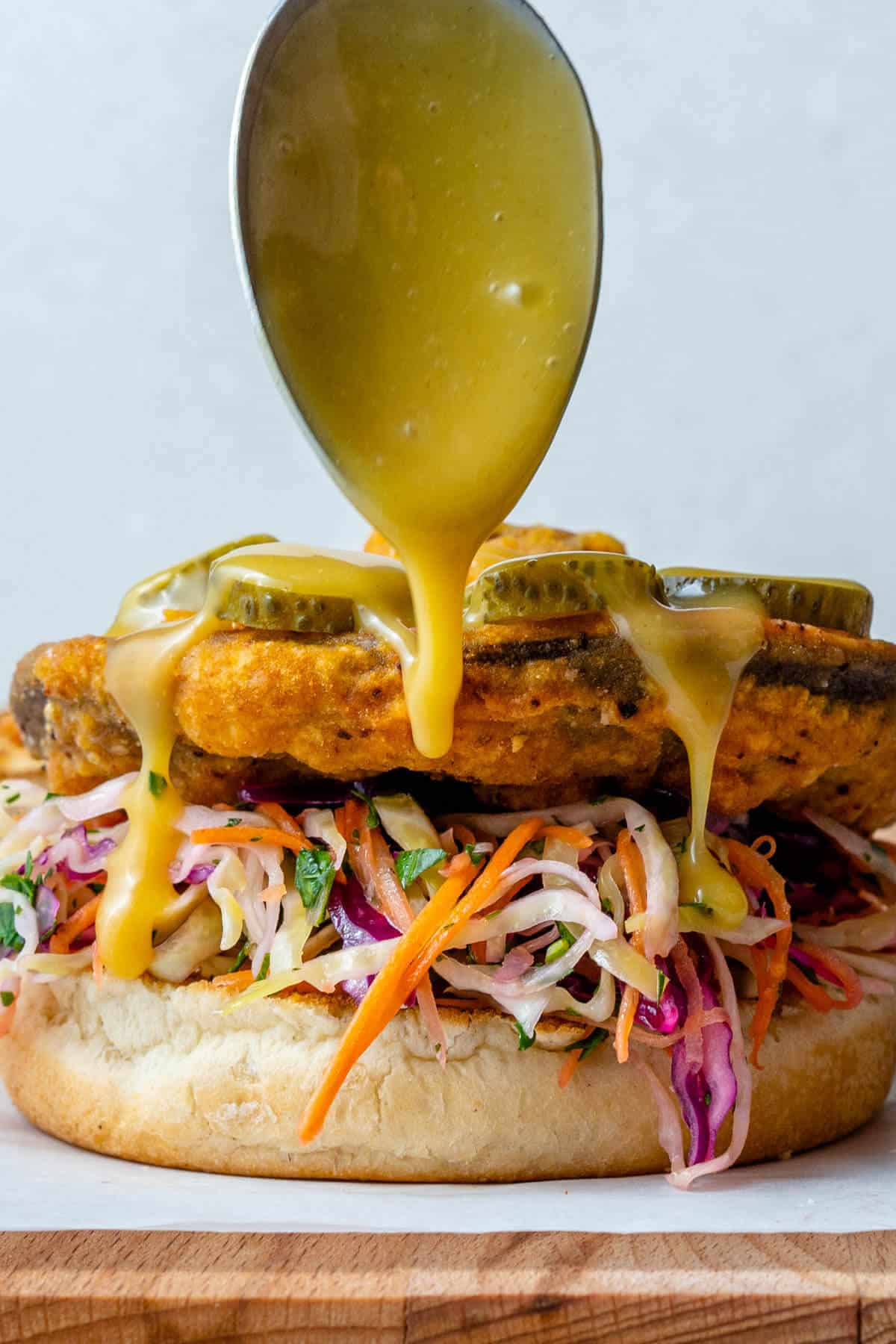 Honey mustard dressing being drizzled on top of vegan chicken sandwich