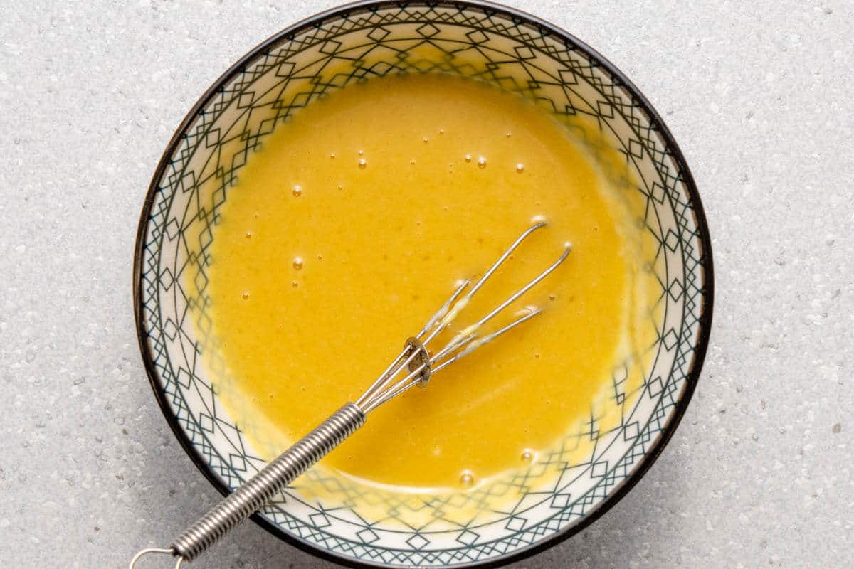 Honey mustard dressing in a small bowl with a whisk