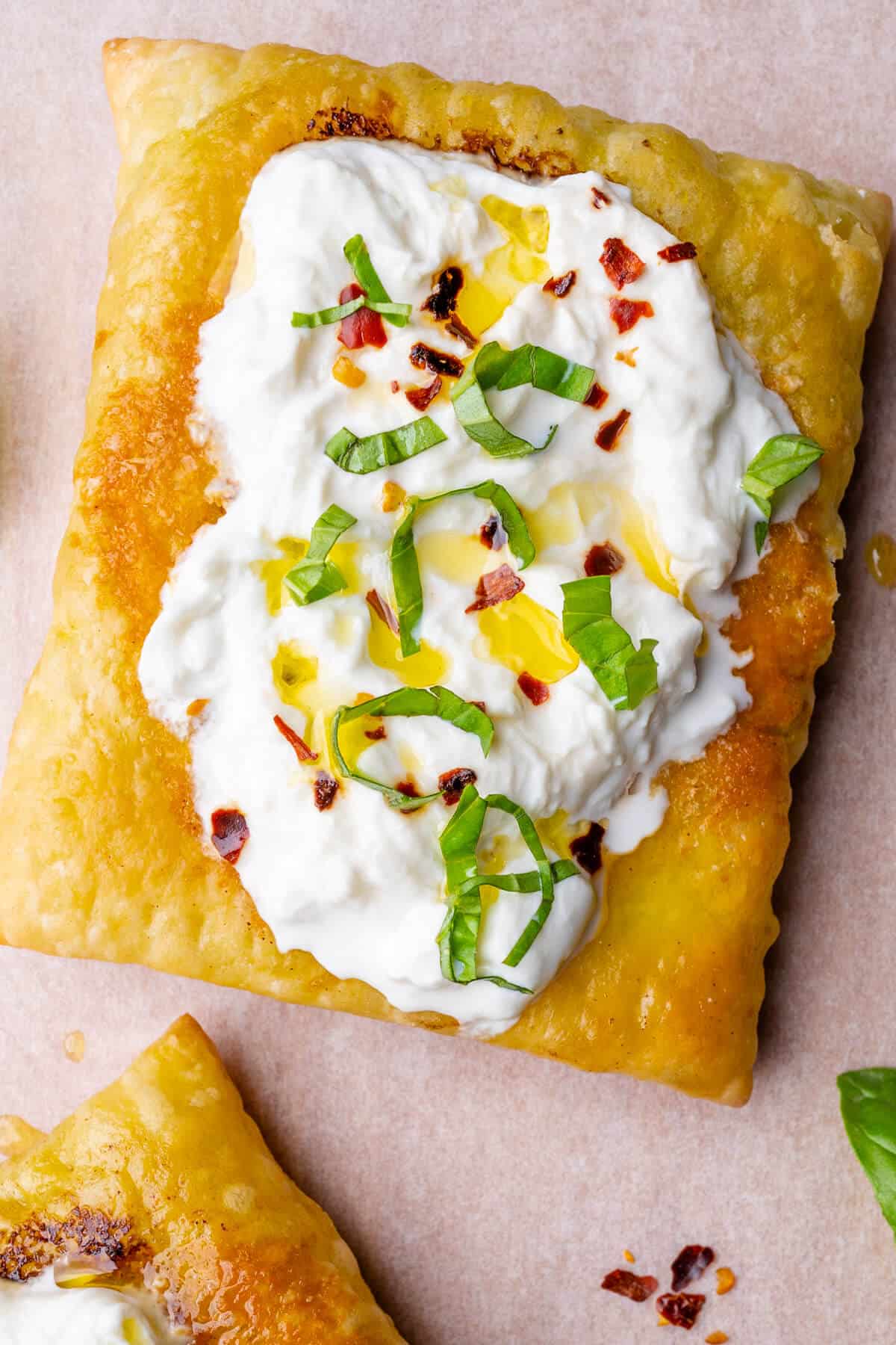 Close up of upside down puff pastry topped with stracciatella, chilli and fresh basil