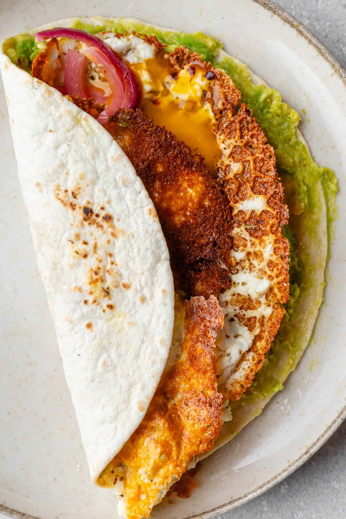 Tortilla folded over to show the layers of avocado and the crispy feta fried egg