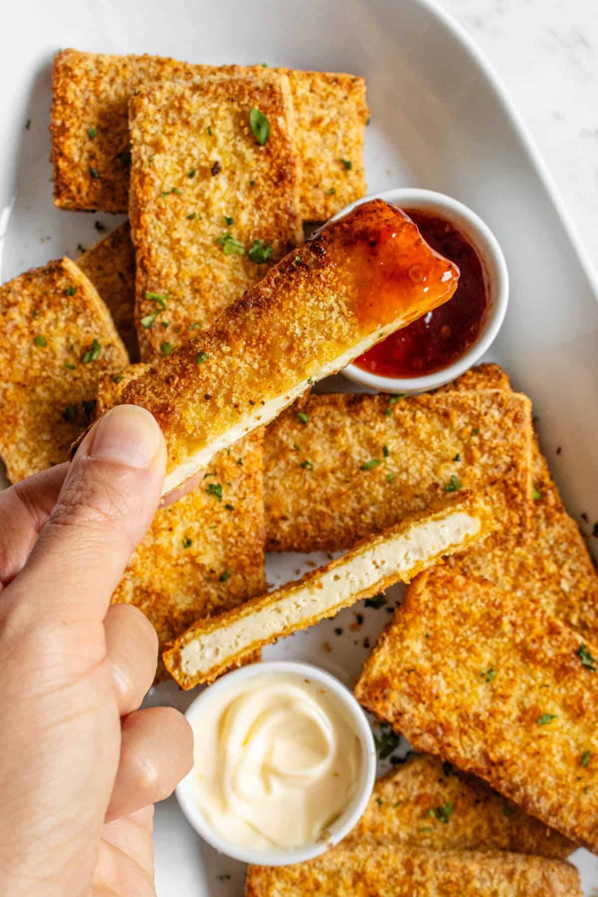 Piece of breaded tofu being dipped in sweet chilli sauce