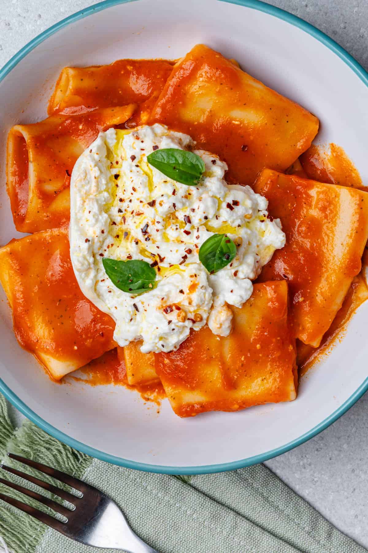A bowl of tomato paccheri pasta with burrata cheese on top