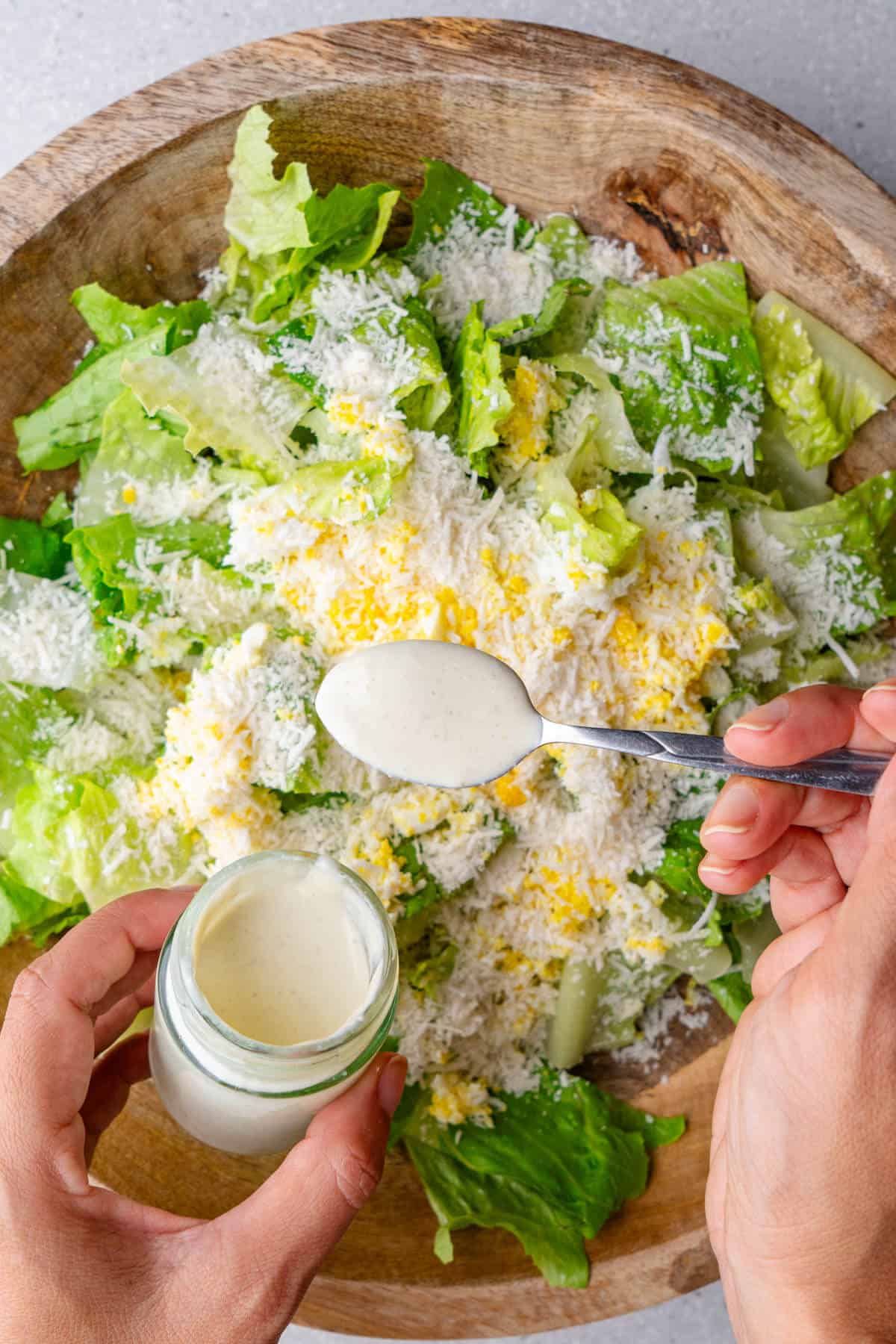 Spoon of caesar salad dressing being poured on top of a salad