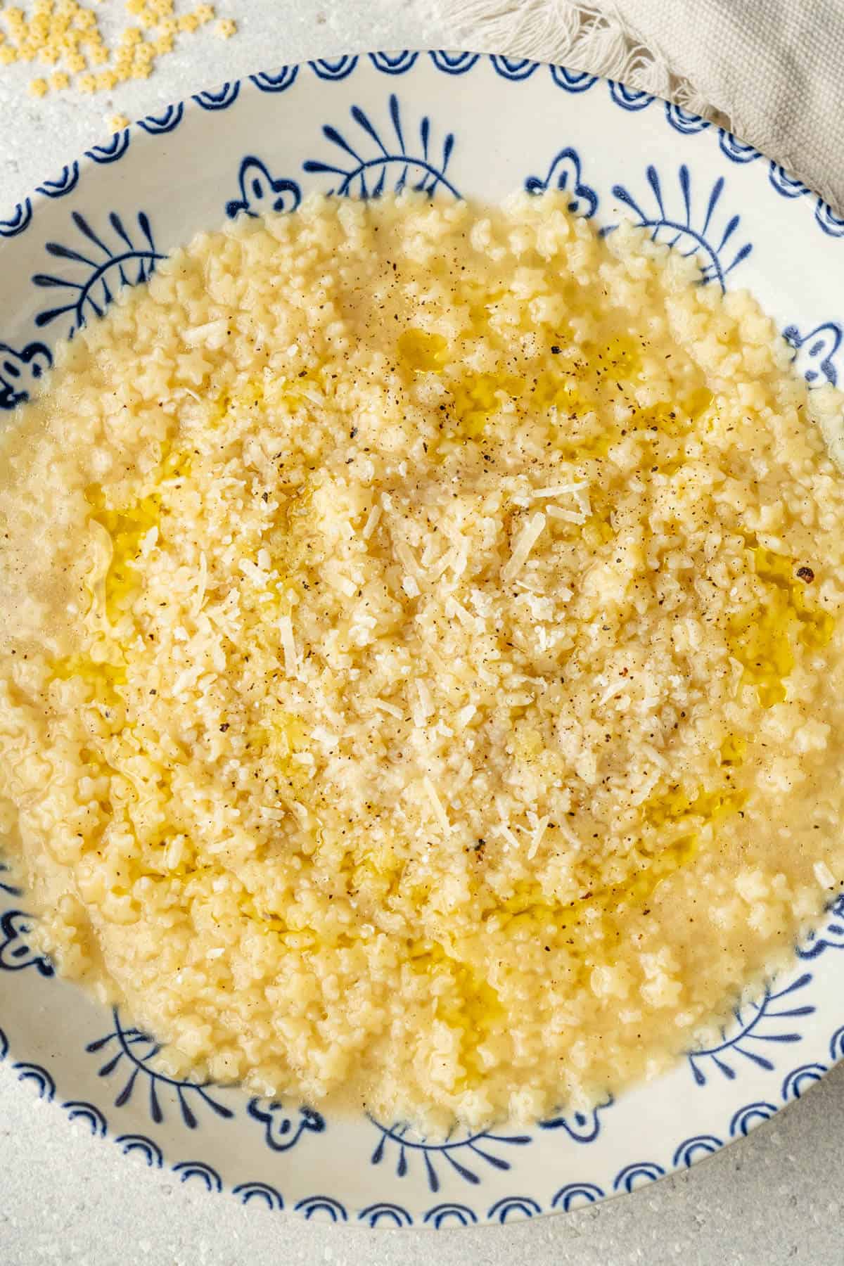 Pastina served in a bowl topped with parmesan, black pepper and drizzle of olive oil