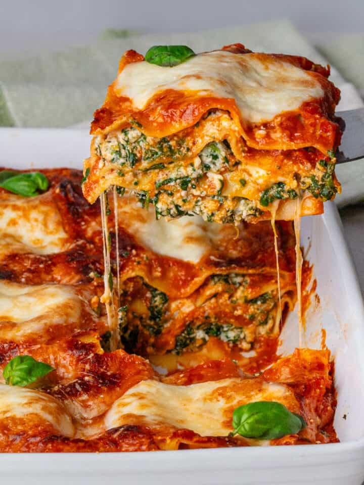 Piece of spinach lasagna being pulled out of an oven dish