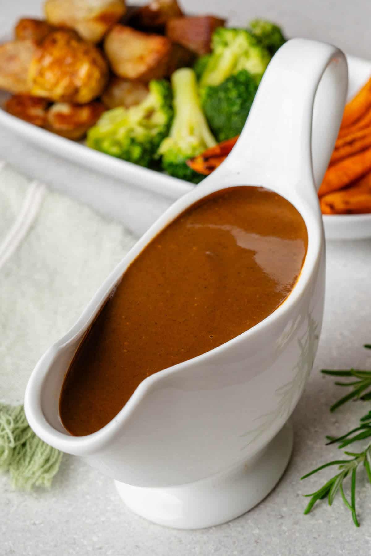 Vegan gravy in a pourer with roasted vegetables on the side