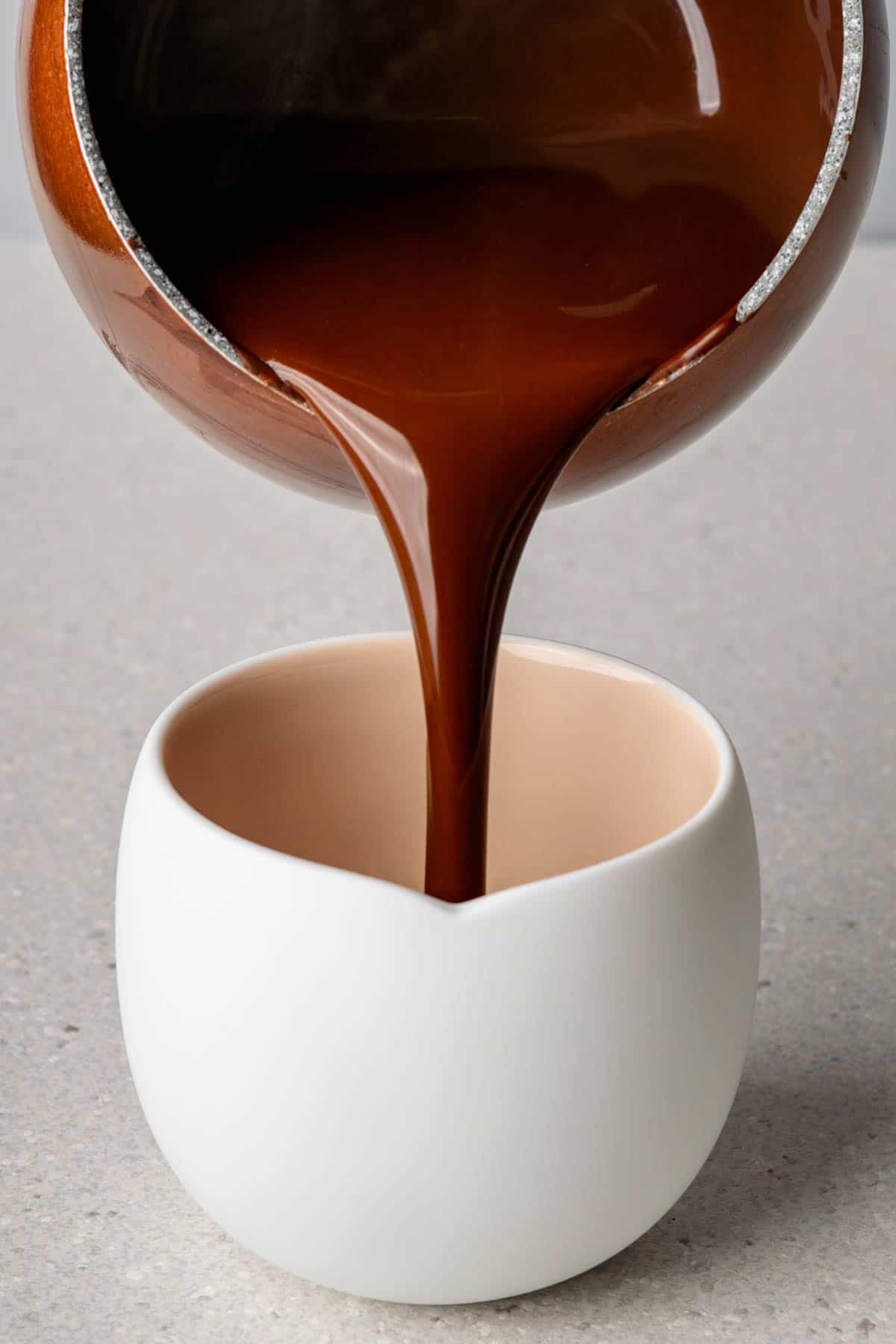 Thick hot chocolate being poured into a white mug
