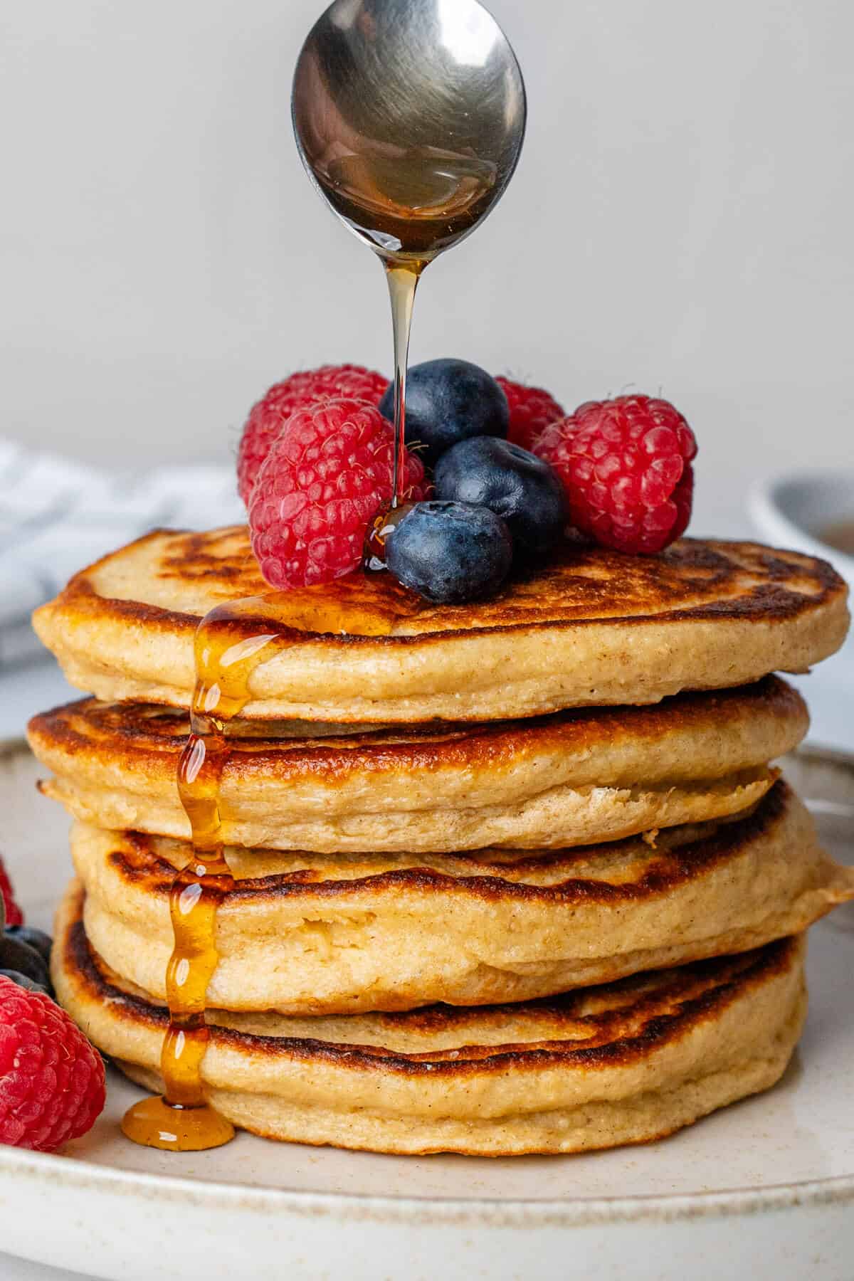 Maple syrup being poured over a stack of Greek yogurt pancakes