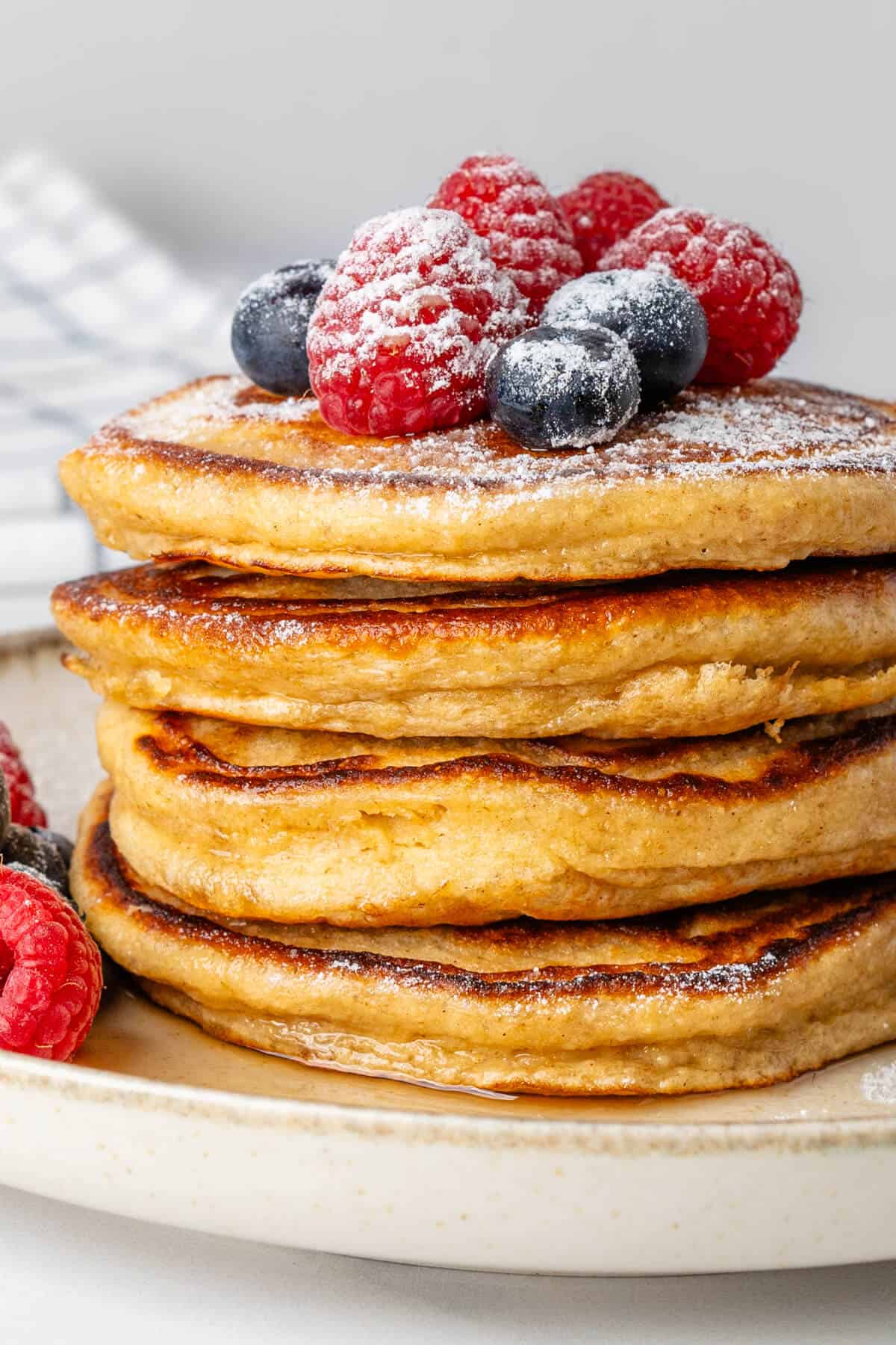 Stack of Greek yogurt pancakes with fresh berries, icing sugar and maple syrup