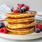 Stack of Greek yogurt pancakes topped with fresh berries, maple syrup and icing sugar