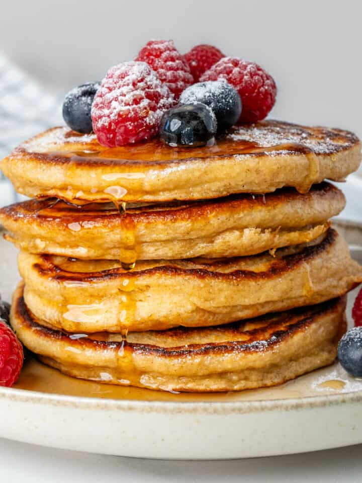 Stack of Greek yogurt pancakes topped with fresh berries, maple syrup and icing sugar