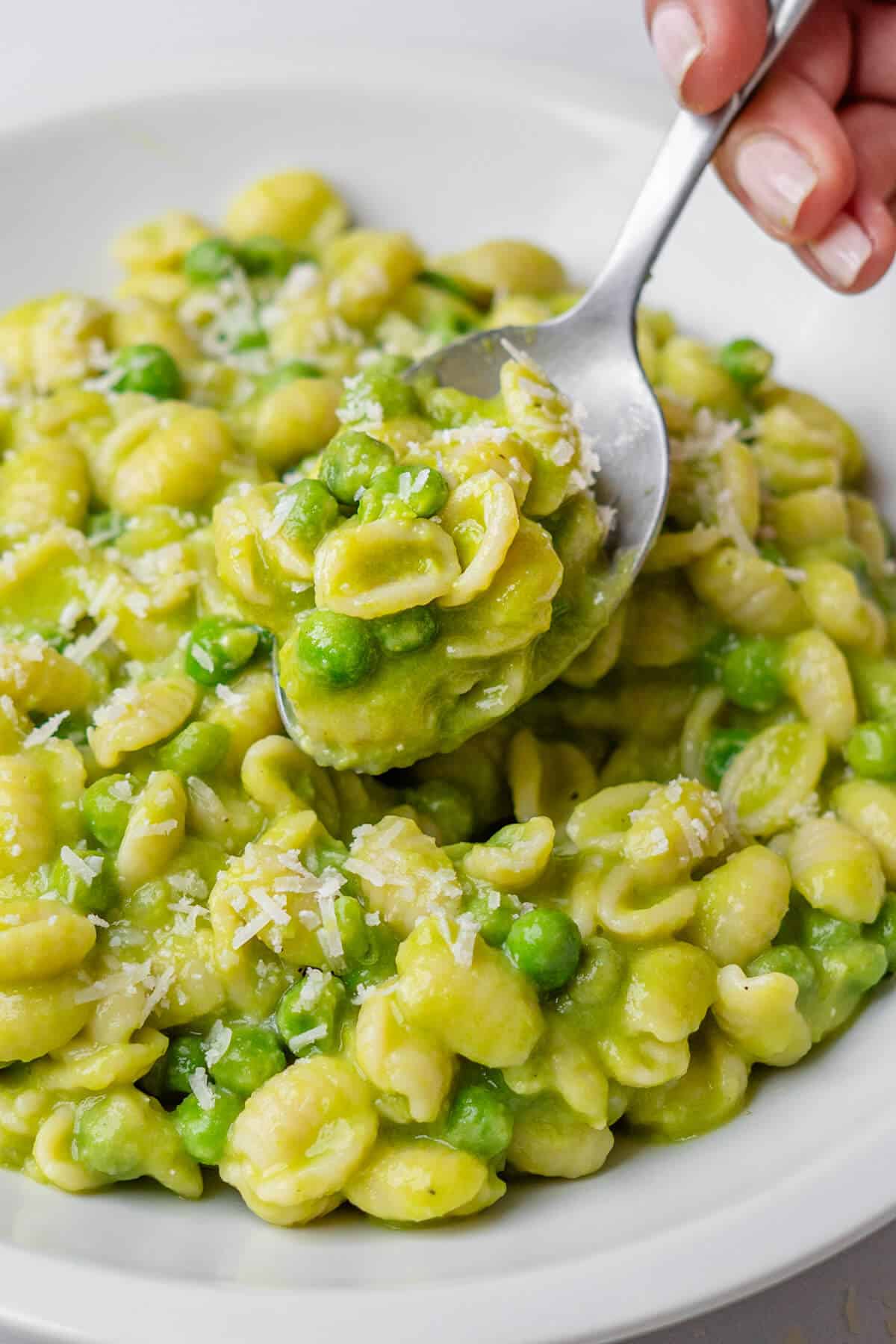 Spoon of pasta with peas coming out of a bowl