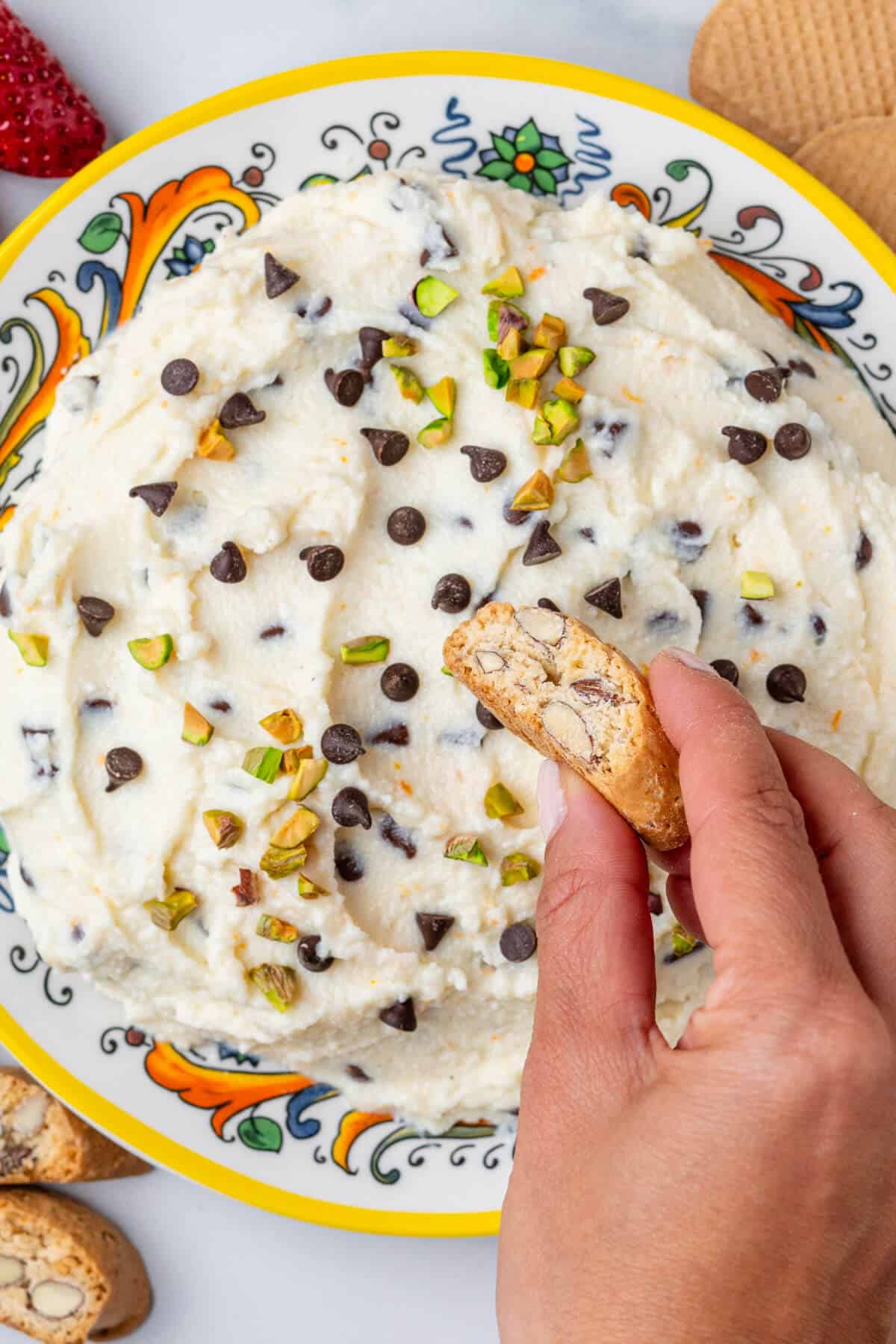 Biscotti being dipped into a a plate of cannoli dip