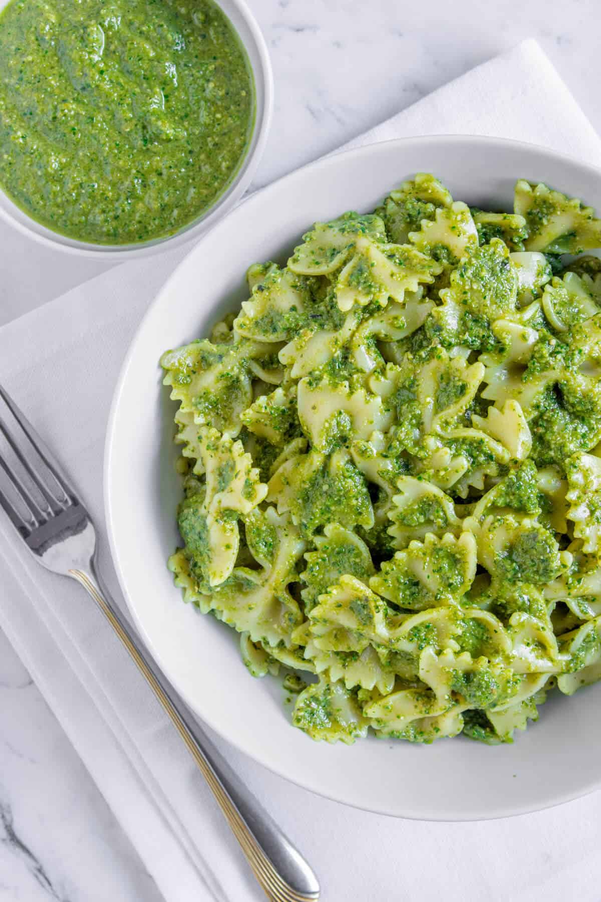 Green pasta served in a bowl with pesto on the side