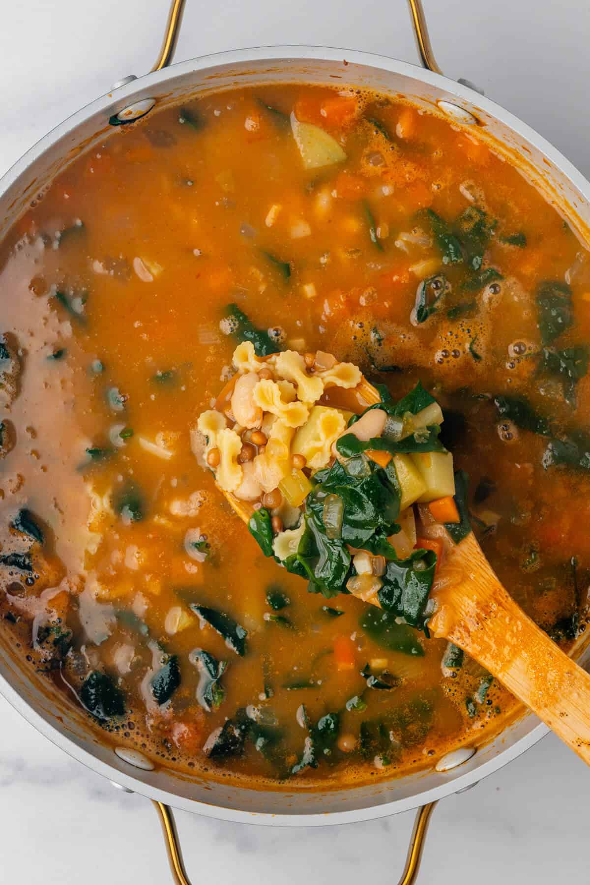 Minestrone soup in a large pot with a wooden spoon