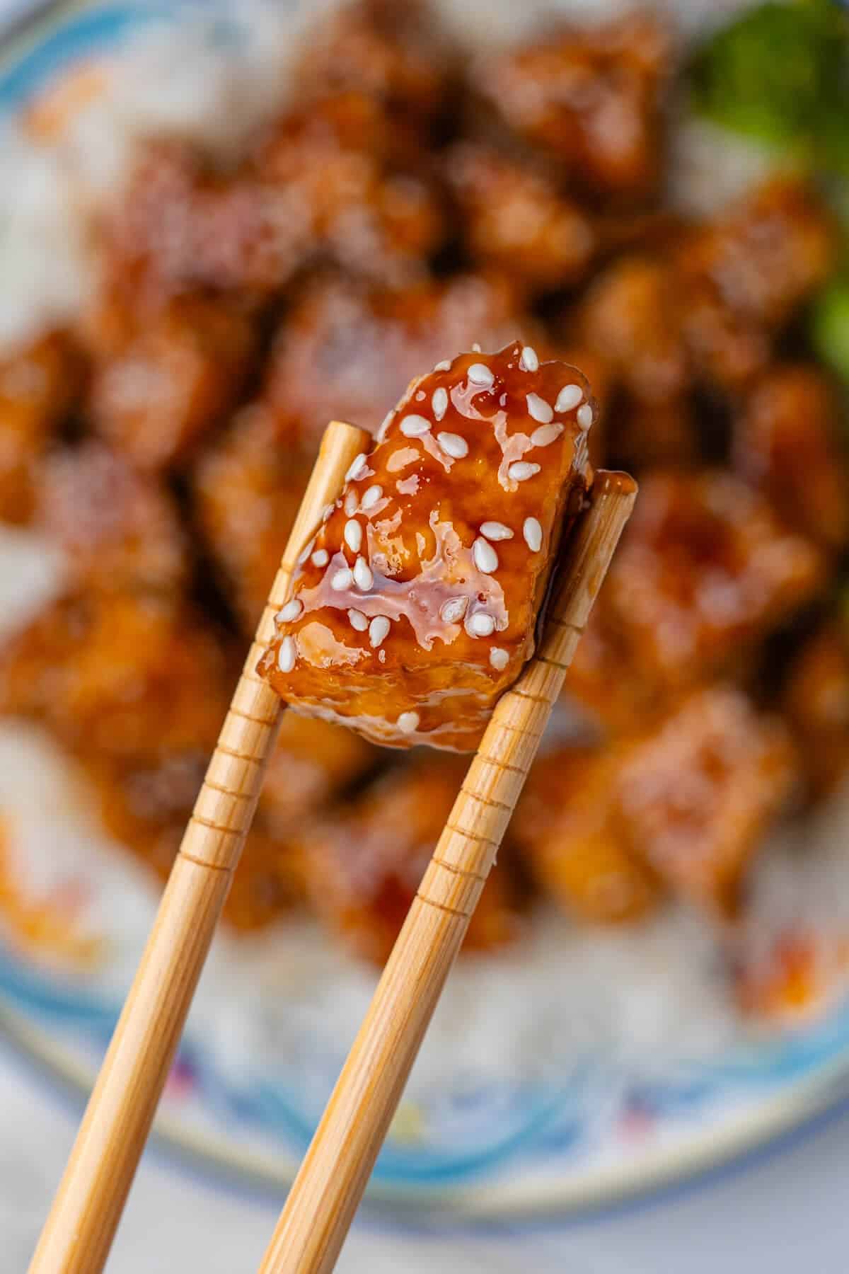 Close up of tofu piece being held with chop sticks