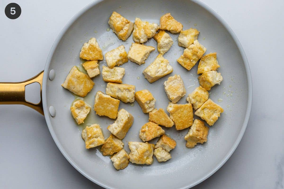 Tofu being fried on a pan with olive oil