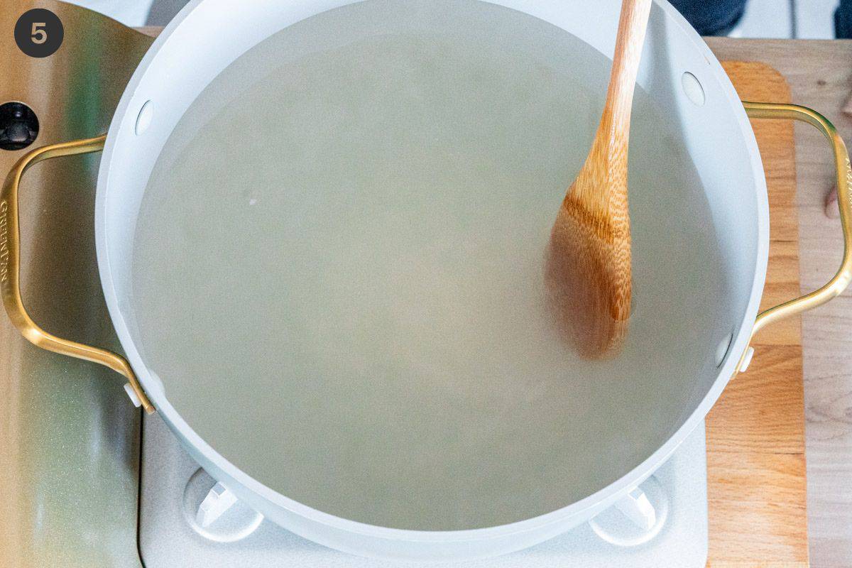 Mixing wooden spoon with sugar and water in a pot