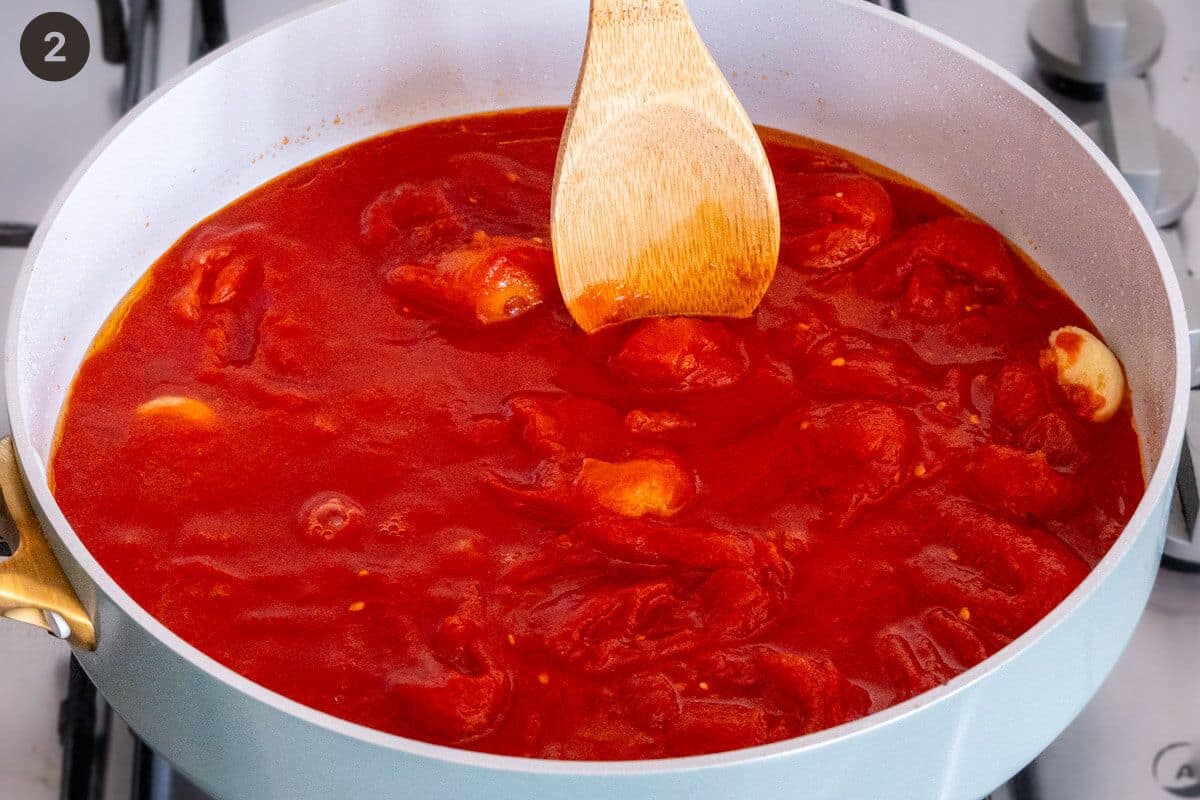 Wooden spoon crushing tomatoes in a pan