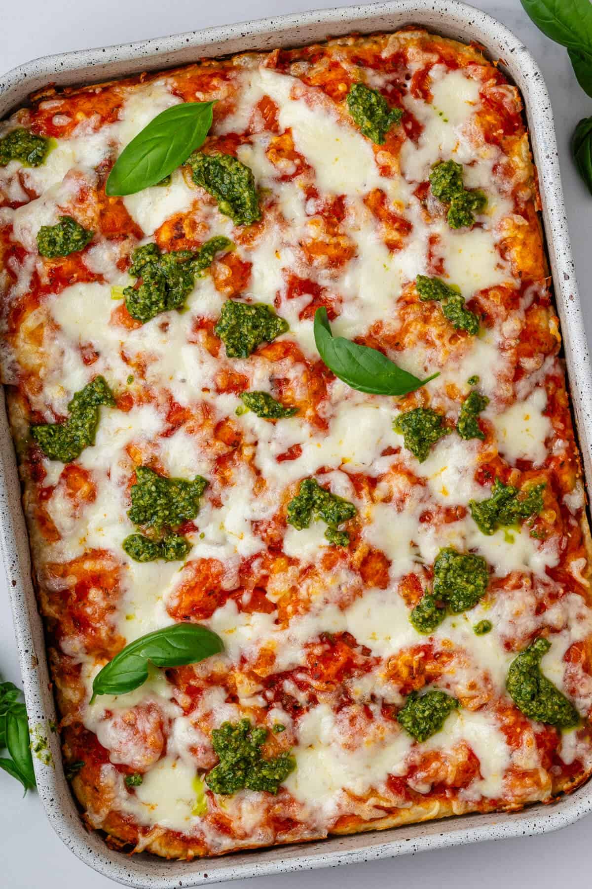 Focaccia pizza in a oven tray topped with fresh basil and pesto