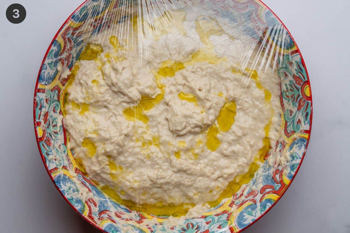 Dough topped with olive oil and plastic wrap before resting