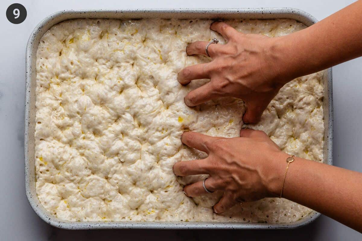 Hands dimpling the dough in an oven tray