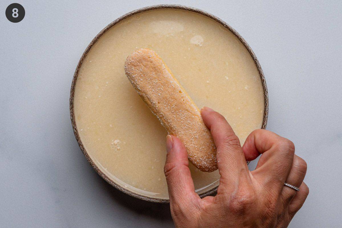 Ladyfinger biscuit being dipped into soaking mixture