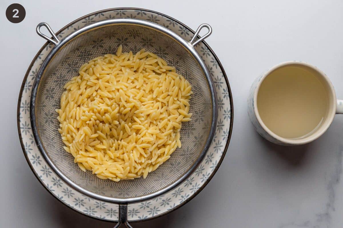 Cooked orzo drained with pasta water saved in a mug