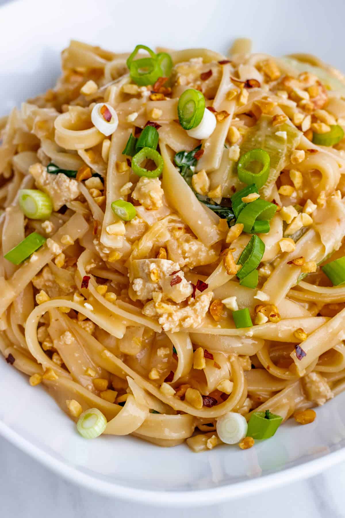 Peanut noodles in a bowl topped with green onions and crushed peanuts