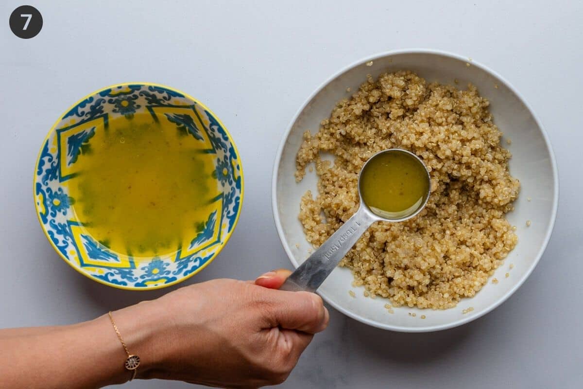 Tablespoon of dressing being poured into a bowl of quinoa