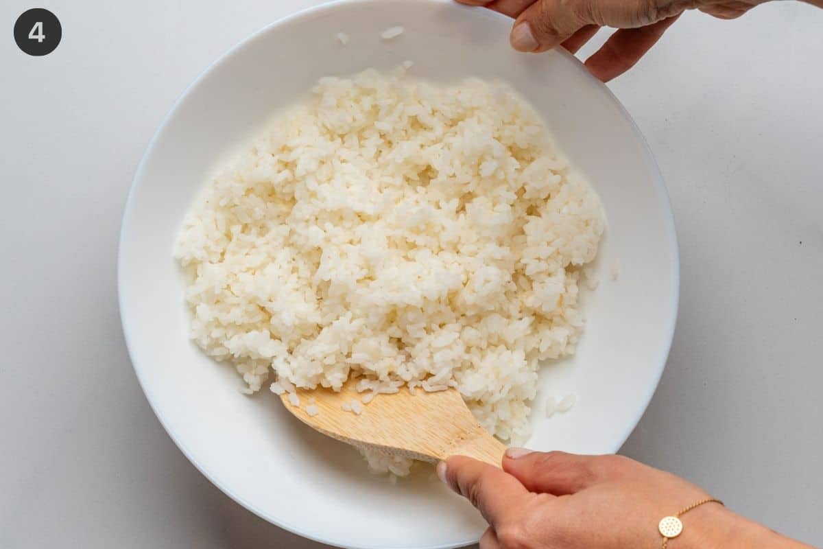 Sushi rice being mixed with a wooden spoon in a bowl