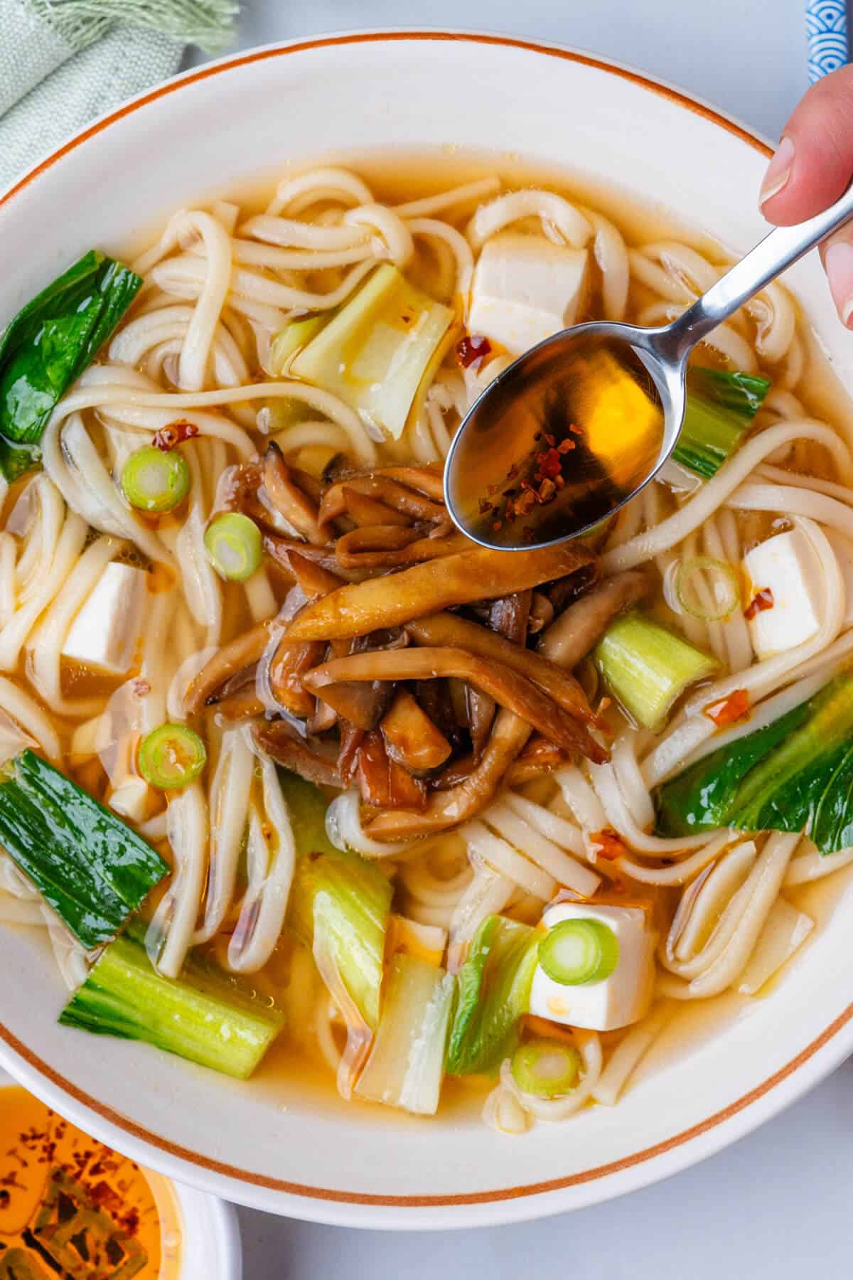 Spoon of chili oil being poured on top of soup bowl