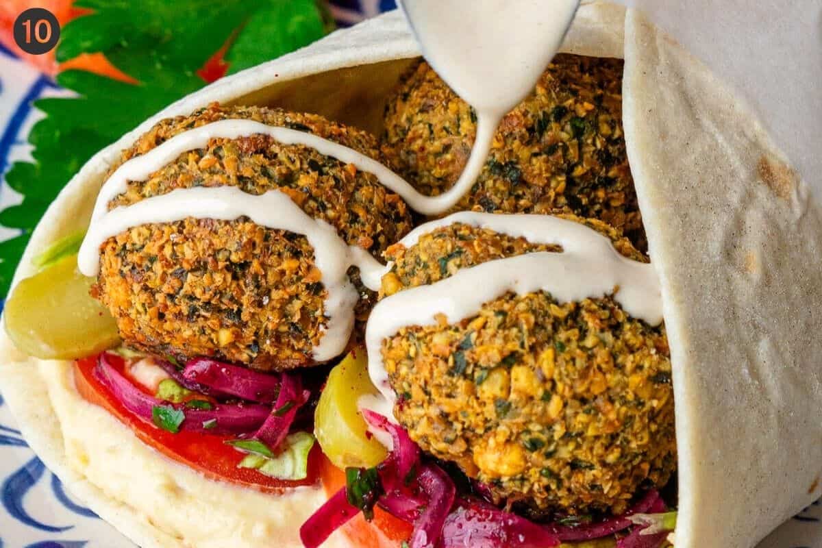 Tahini sauce being drizzled over a falafel wrap