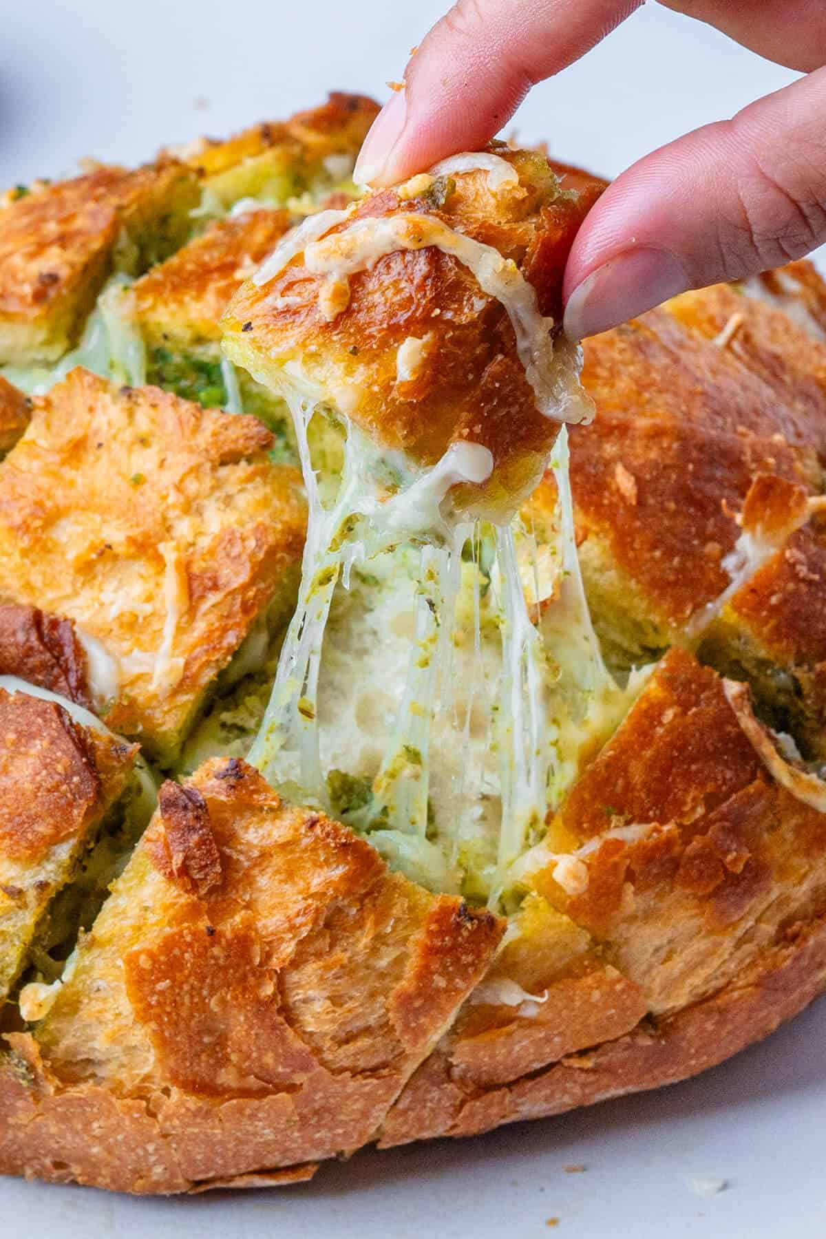 Piece of cheesy bread being pulled out of the loaf