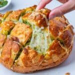 Cheesy pull apart bread with pesto with a piece being pulled out